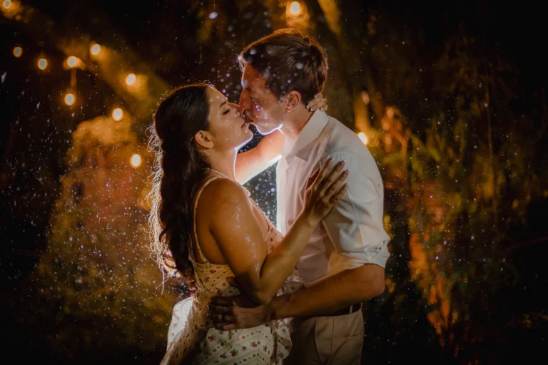 Fotografía de bodas de una pareja de novios bajo la lluvia, con las gotas iluminadas a contraluz. Retrato editorial que combina luz dramática, composición artística y un estilo documental.