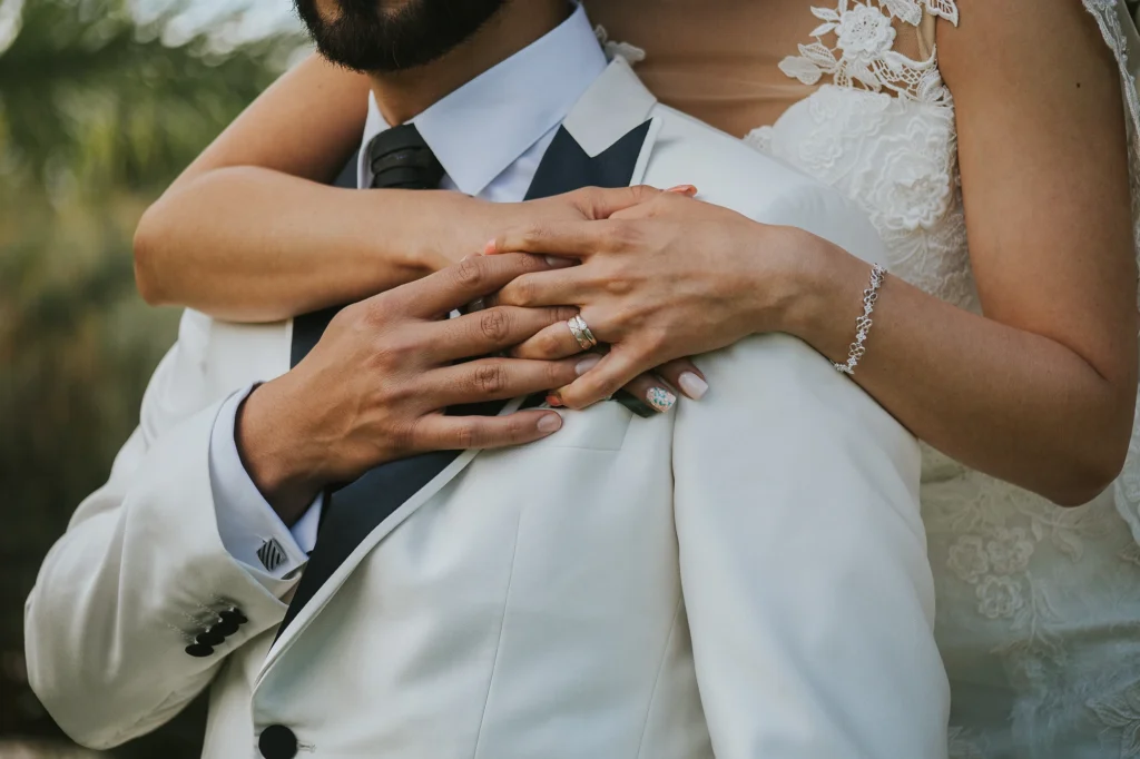 Primer plano de las manos de los novios entrelazadas mostrando sus anillos de matrimonio durante el día de su boda.