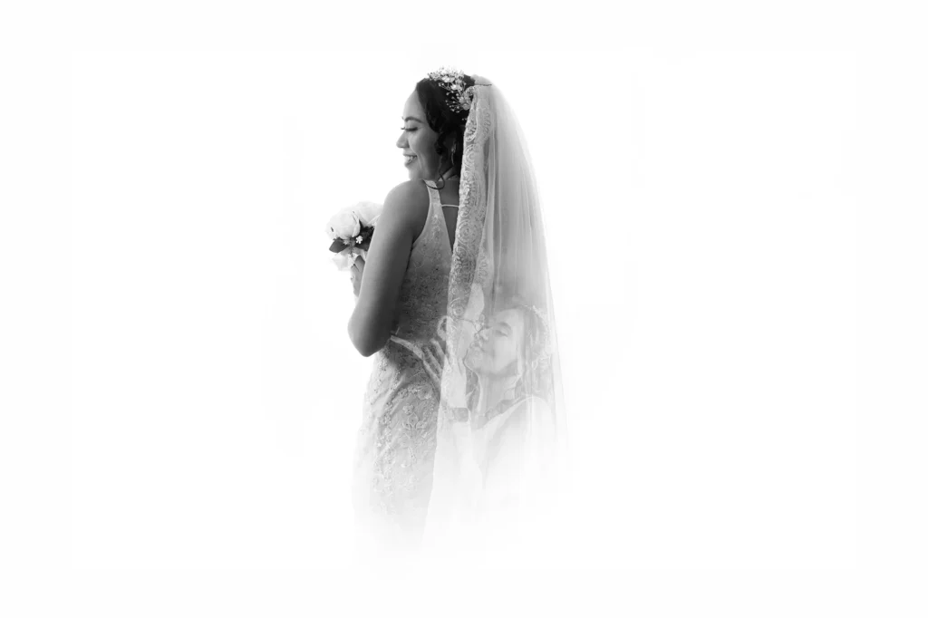 Fotografía de bodas con doble exposición que muestra a una novia de espaldas mientras su velo revela a la pareja dándose un beso. Retrato editorial con composición artística y luz natural.