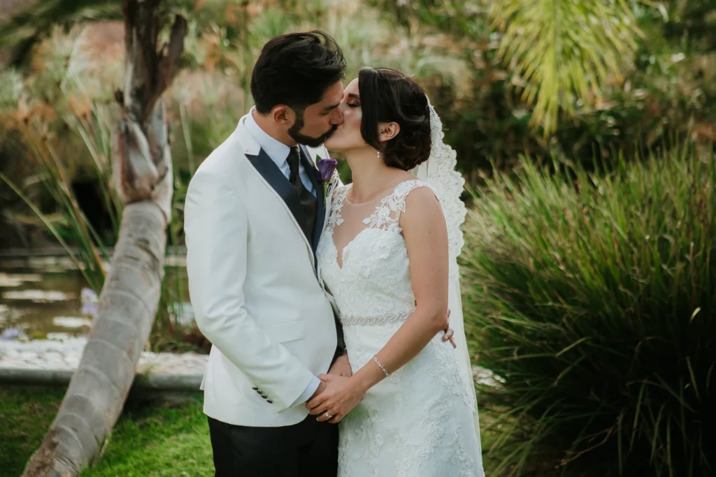 Novios recién casados se besan en un hermoso jardín rodeado de naturaleza durante su sesión de fotos de boda.