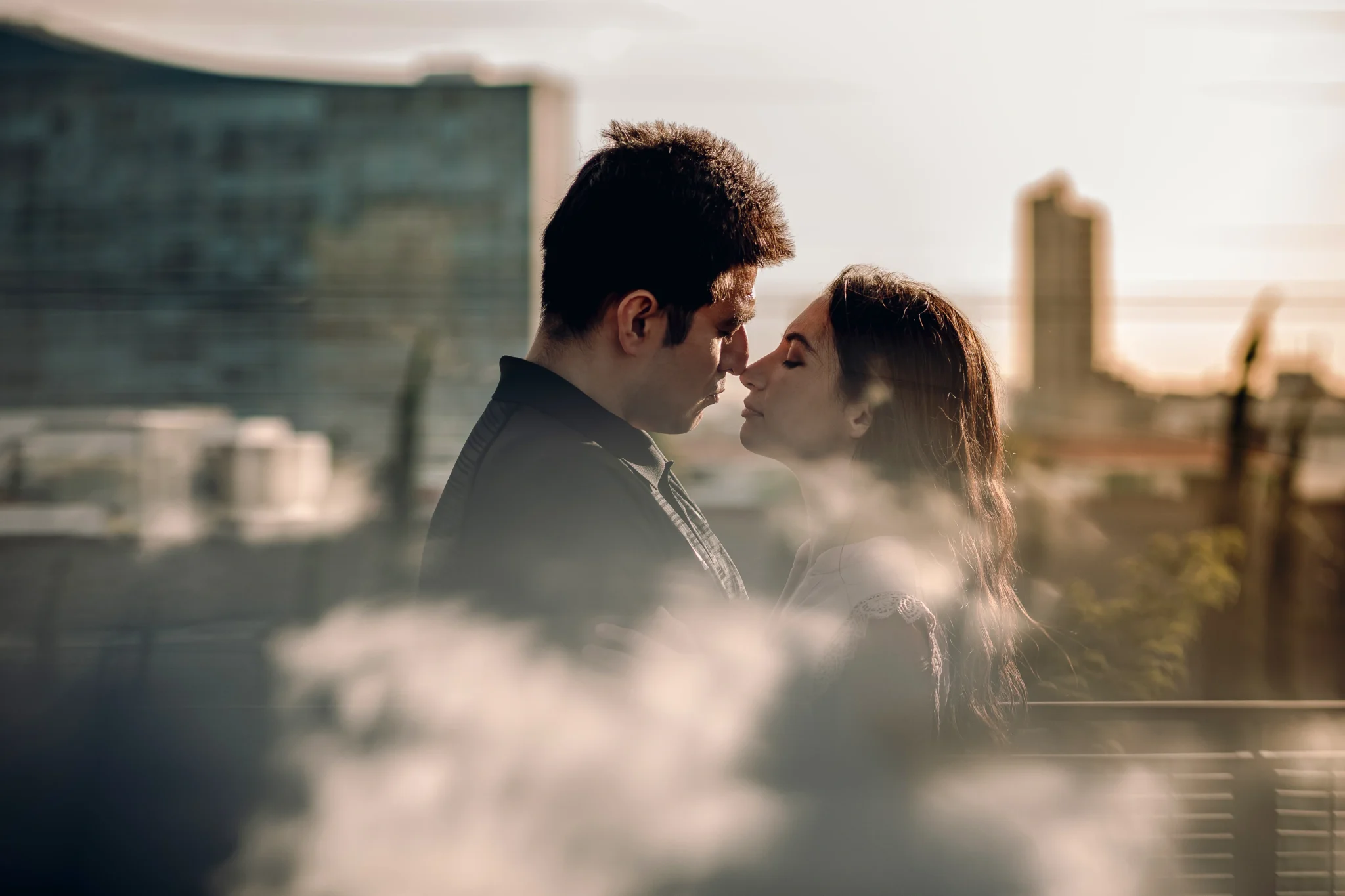 Fotografía editorial de una pareja rozando sus narices con la ciudad de fondo, capturada con luz natural y composición cinematográfica para resaltar la conexión y las emociones.