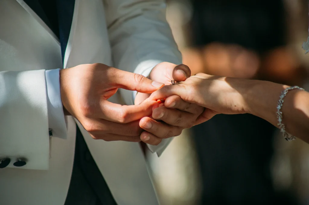 Primer plano de las manos del novio colocando el anillo de matrimonio en la mano de la novia durante la ceremonia de boda.