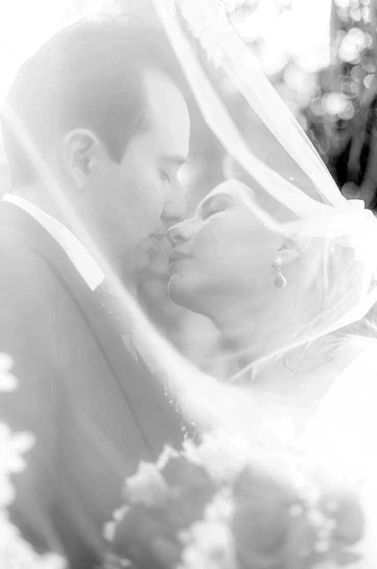Retrato de novios dándose un beso detrás del velo de la novia. Fotografía de bodas editorial que utiliza la transparencia del velo, la luz natural y una composición artística para crear una imagen elegante y atemporal.