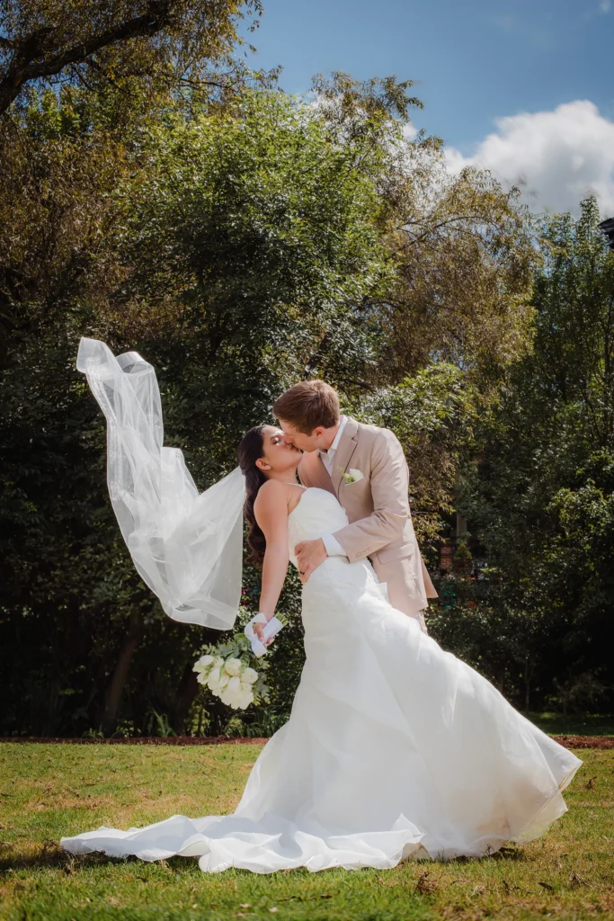 Fotografía profesional de bodas donde el novio sostiene a la novia hacia atrás mientras el velo vuela con el viento. Retrato editorial con movimiento, luz natural y una composición artística llena de elegancia.