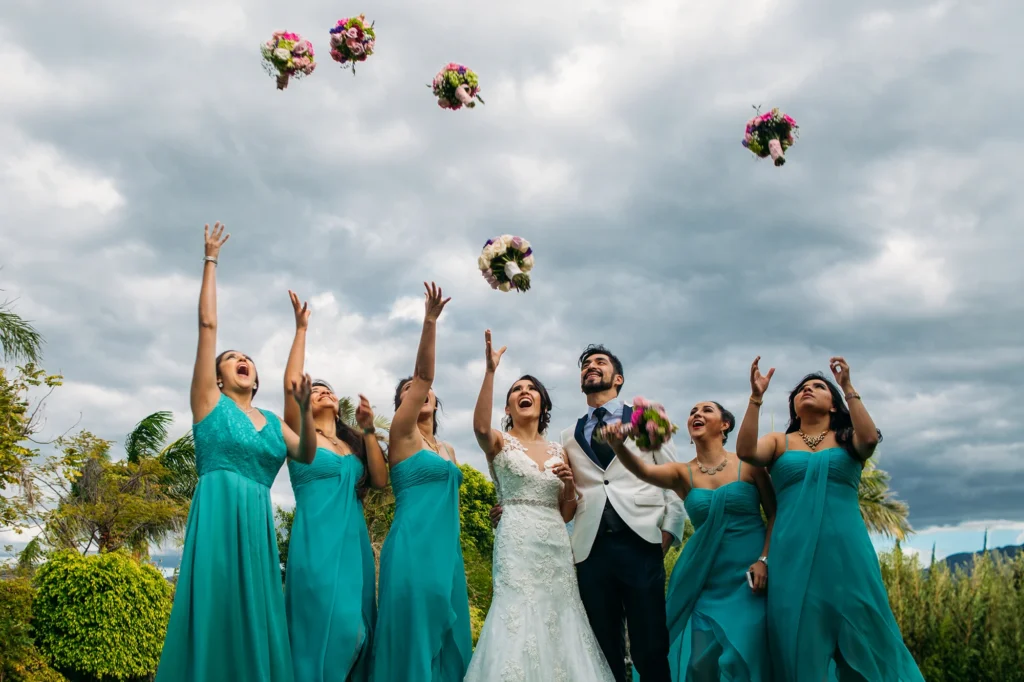 La novia y sus damas de honor celebran con entusiasmo mientras lanzan el ramo durante la recepción de la boda, capturando un momento lleno de felicidad, amistad y emoción.